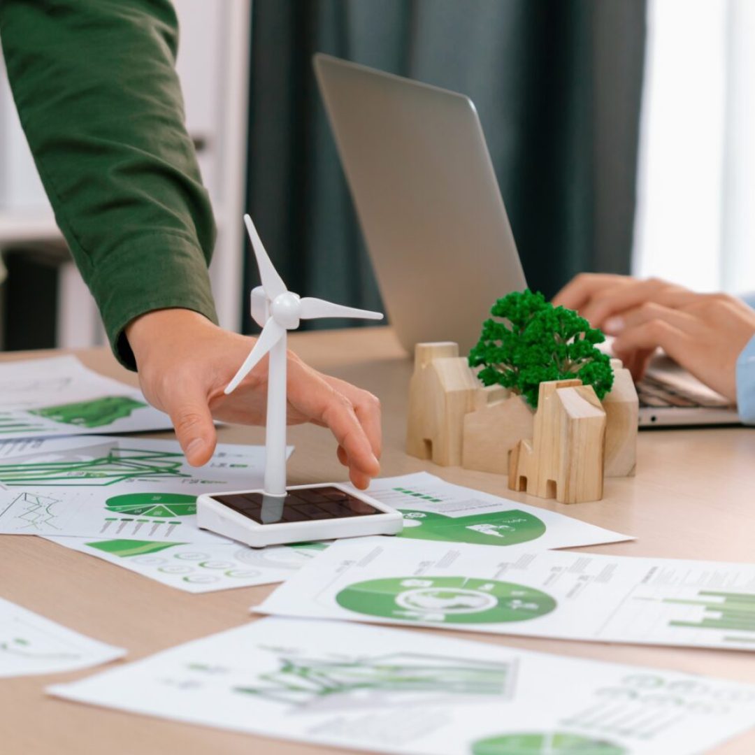 Windmill model represented renewable energy and wooden block represented eco city was placed on green business meeting table with environmental document scatter around. Front view. Delineation.
